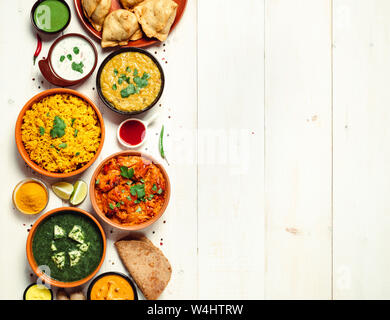 Indische Küche Gerichte: Tikka Masala, dal, Paneer, Samosa, chapati, Chutney, Gewürze. Indische Küche auf weißem Holz- Hintergrund. Sortiment indische Mahlzeit mit Kopie Platz für Text. Top View oder flach. Stockfoto