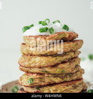 Zucchini Krapfen. Glutenfreie zucchini Krapfen im Stapel auf weißem Hintergrund. Gemüse zucchini Pfannkuchen oder Krapfen mit Frühlingszwiebeln und Parmesan Käse, dazu saure Sahne oder griechischer Joghurt Stockfoto