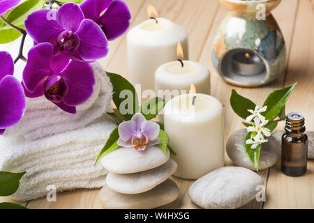 Komposition mit Orchideen und Jasmin, einige kleine Flaschen mit ätherischem Öl, Kerzen und Licht Steine für Massage Stockfoto