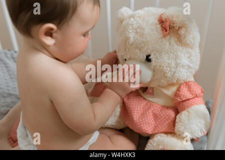 Baby Mädchen spielen mit einem Teddybär in einer Krippe. Stockfoto