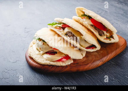 Gegrilltes Rindfleisch Burger im Fladenbrot mit Sauce, Käse, Tomaten und Rucola Blätter Stockfoto