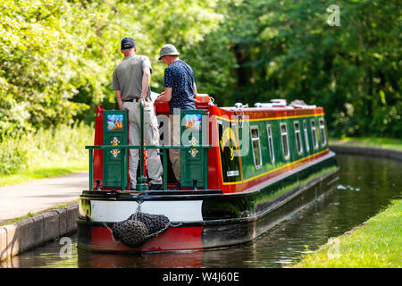 Ansicht der Rückseite zwei Männer auf dem Heck eines schmalen Boot Navigieren entlang eines Kanals an einem sonnigen Sommertag, UK. Stockfoto
