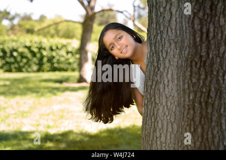 Ein Mädchen versteckt sich hinter einem Baum Stockfoto