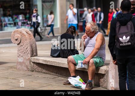 SHEFFIELD, UK - 20. JULI 2019: Ein älterer übergewichtiger weißer Mann in einem Tanktop sitzt auf einer Bank in der Stadt essen eine Greggs pasty Stockfoto