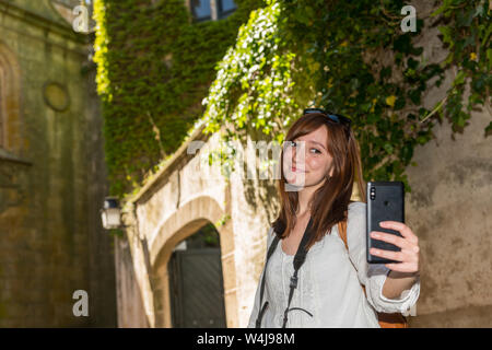 Eine junge Rothaarige touristische macht einen selfie Neben einem Turm in grün Efeu in der Altstadt von Caceres abgedeckt Stockfoto