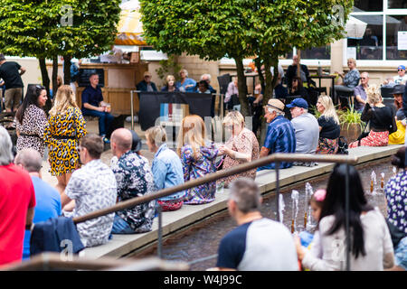 SHEFFIELD, UK - 20. JULI 2019: Massen von Menschen sitzen in einem Quadrat in Sheffield City Centre für die Fahrgassen gerade eine Band spielen Stockfoto