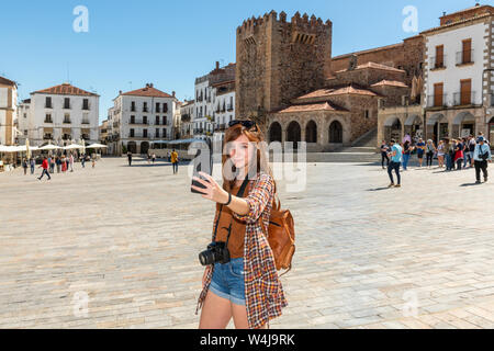 Eine junge Rothaarige Tourist mit einem Rucksack macht einen selfie auf der Plaza Mayor de Caceres Stockfoto