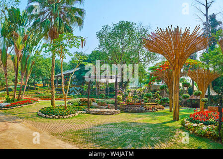 Die Gasse der Mae Fah Luang Garten mit hohen Palmen, Blumenbeete, Sträucher beschnitten, Bambus Sonnenschirme und traditionellen Akha Hill Tribe swi Stockfoto