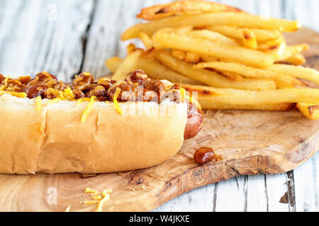 Hot Dog mit Chili, Cheddar Käse und Senf. Selektiver Fokus mit Pommes frites in der Hintergrund verschwommen. Stockfoto