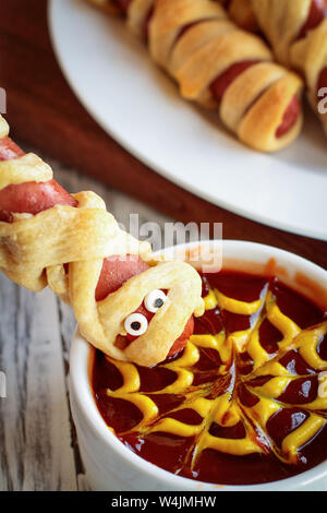 Spaß Essen für Kinder. Mama hot dogs hielt den Kopf über eine Schüssel mit Ketchup und Senf dip, mit spider web design. Stockfoto