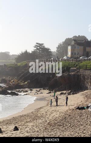Vertikale Aufnahme einer Familie, die am Strand steht In der Nähe einer Klippe mit Gebäude oben Stockfoto