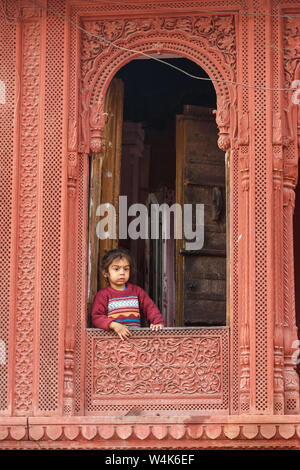 Bikaner, Indien - 11. Februar 2019: indische Mädchen in Holz geschnitzte Fenster in der Altstadt von Bikaner. Rajasthan Stockfoto