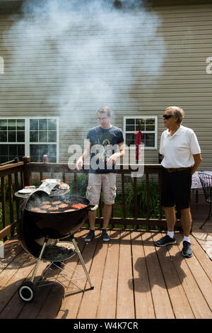Ein Mann beaufsichtigt sein Enkel wie er kocht das Abendessen auf dem Grill an einem schönen Sommertag in einem Vorort von Indianapolis, Indiana, USA. Stockfoto