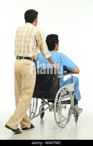 Stationsjunge, der einen Patienten auf einen Rollstuhl schiebt Stockfoto