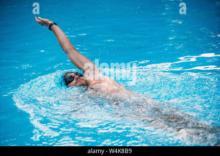 Athletischen jungen Mann Schwimmen auf Rückschlag Stil. Schwimmen Wettbewerb. Stockfoto