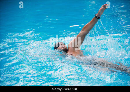 Athletischen jungen Mann Schwimmen auf Rückschlag Stil. Schwimmen Wettbewerb. Stockfoto