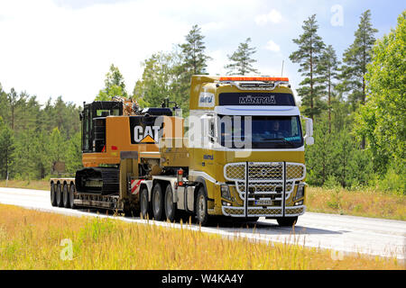 Raasepori, Finnland. Juli 5, 2019. Volvo FH 16 Auflieger von E&E Mantyla Ky hols Cat 325 F Hydraulikbagger entlang der Finnischen Landstraße 25 im Sommer. Stockfoto