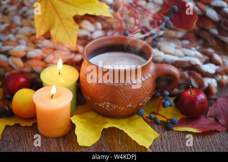 Gemütliche herbst Zusammensetzung mit einer Tasse heißen Kaffee, Kerzen, Herbstlaub und Schal auf einer hölzernen Hintergrund Stockfoto