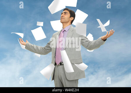 Papiere, die auf einen Geschäftsmann fallen, der mit ausgestreckten Armen steht Stockfoto