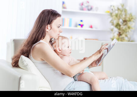 Glückliche Mutter ein Jahr altes Baby Holding auf seinen Händen und zeigt ihr Bild auf digital Tablet Stockfoto