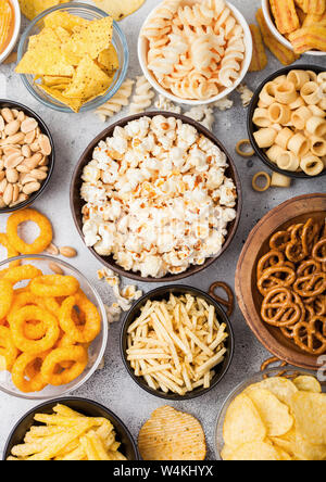 Alle klassischen Kartoffel Snacks mit Erdnüssen, Popcorn und Zwiebelringen und gesalzene Brezeln in Schüssel Platten auf Leuchtkasten. Twirls mit Stöcken und Kartoffelchips Stockfoto