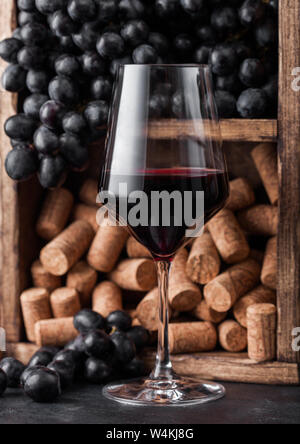 Eleganten Glas Rotwein mit dunklen Trauben und Korken in vintage Holzkiste, die auf dem schwarzen Stein. Stockfoto