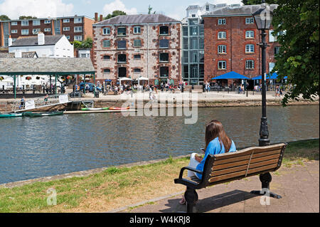 Junge Frau auf einer Bank am Ufer des Flusses Exe in Exeter, Devon, England, Großbritannien, Großbritannien. Stockfoto