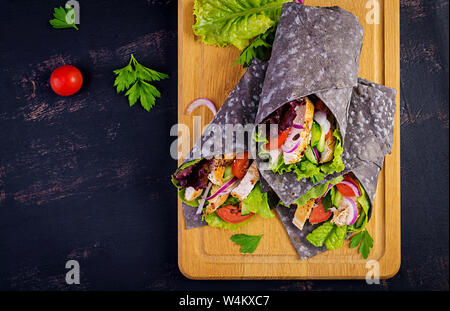 Tortilla mit Tinte Tintenfisch Wraps mit Hähnchen und Gemüse auf schwarzem Hintergrund. Chicken burrito, mexikanisches Essen. Ansicht von oben Stockfoto