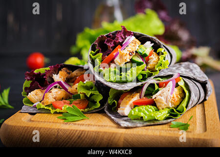 Tortilla mit Tinte Tintenfisch Wraps mit Hähnchen und Gemüse auf schwarzem Hintergrund. Chicken burrito, mexikanisches Essen. Stockfoto