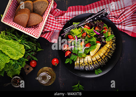 Geräucherte Makrele und frischen Salat auf dunklem Hintergrund. Ansicht von oben Stockfoto