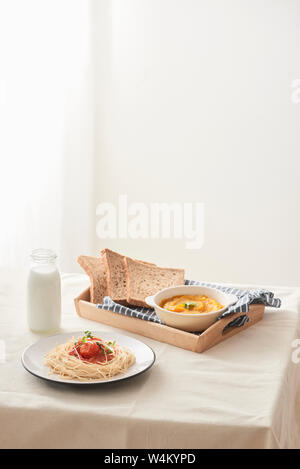 Hausgemachte Spaghetti mit Tomatensauce in einem weißen Teller auf dem Tisch mit kürbispüree, Milch und Toast. Stockfoto