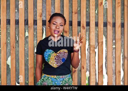 Junge afrikanische amerikanische Frau gegen die Holzwand gestellt, blinkenden Augen und zwei Finger zeigen. Stockfoto