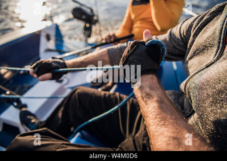 Des Menschen Hand mit Boot Seil. Yachtsman Mauren seinen Motor Boot am Steg. Nahaufnahme, Hände und Bug des Bootes. Stockfoto