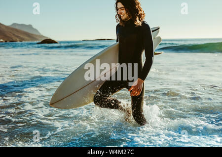 Junger Mann mit Surfbrett am Strand. Mann aus dem Meer nach Wasser surfen. Stockfoto