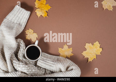 Gestrickte Pullover, Tasse Kaffee, Herbst Ahorn auf braunem Hintergrund bleibt. Flach, Ansicht von oben, kopieren. Frauen Kleidung. Stockfoto