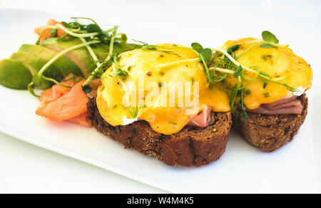 Eier Benedikt auf braunem Brot Toast mit Lachs und Avocado in Scheiben geschnitten Stockfoto