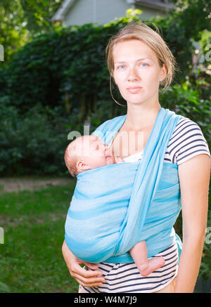 Junge Mutter ihr kleines Baby girl in blue Schlinge im Freien. Kind schläft in Komfort, Sicherheit und Schutz. Stockfoto