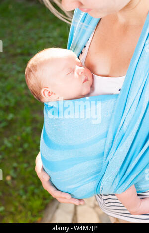 Junge Mutter ihr kleines Baby girl in blue Schlinge im Freien. Kind schläft in Komfort, Sicherheit und Schutz. Stockfoto