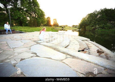 Kleines Mädchen mit ihrer Mutter die Fütterung der Enten in der Nähe von dem See im Park im Sommer Stockfoto