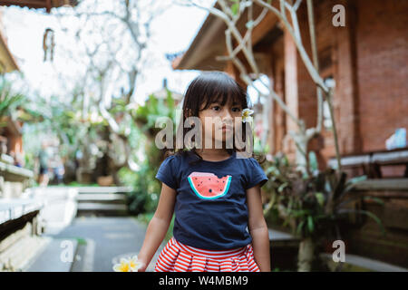 Kleines Mädchen mit Blumen Tragen im Ohr zu Fuß außerhalb des Hauses Stockfoto