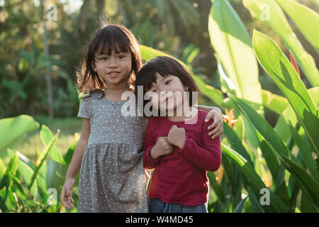 Zwei kleine Mädchen stehen umarmen, während im Park Stockfoto
