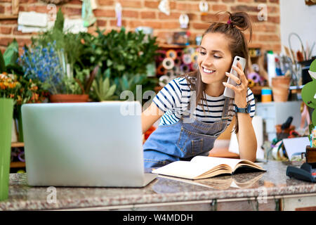 Junge Floristen auf Laptop und Beantworten von Anrufen während lehnte sich auf Counter im Shop Stockfoto