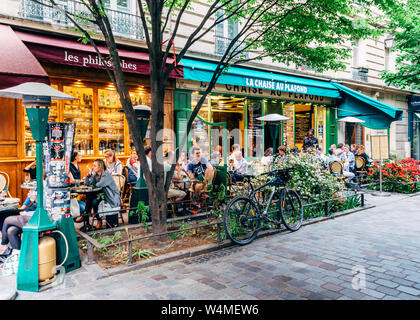 Paris, Frankreich - 8. Mai 2016: Leute, ein Café und ein Gespräch an einem ruhigen und charmanten Baum genießen gesäumten Straße im böhmischen Marais-Viertel von Paris. Stockfoto