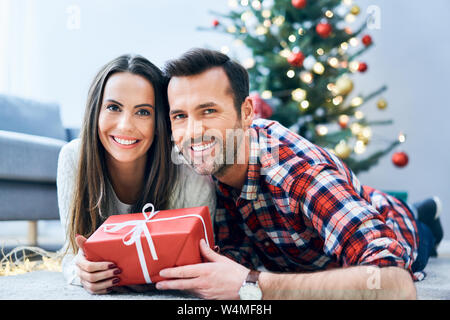 Fotos von lächelnden Paar in die Kamera schaut beim Entspannen im Zimmer tauschen Weihnachtsgeschenk Stockfoto