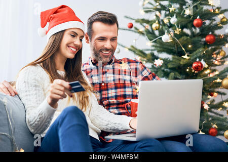 Paar sitzt auf dem Sofa und machen Weihnachtseinkäufe online mit Kreditkarte und Laptop Stockfoto