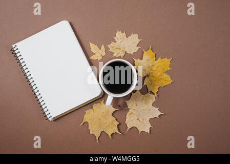 Herbst Komposition. Tasse Kaffee, Notebook, Herbst Ahorn Blätter auf braunen Hintergrund. Flach, Ansicht von oben, kopieren. Stockfoto