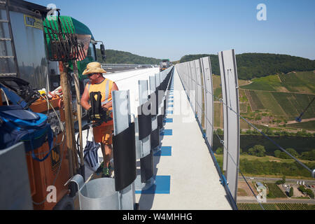 Zeltingen Rachtig, Deutschland. 24. Juli, 2019. Arbeitnehmer Asphalt der Straße Oberfläche des Hochmosel Brücke im Bau bei Temperaturen deutlich über 30 Grad Celsius. Es gibt keine schattigen Platz auf dem 160 Meter hohen Gebäude über dem Moseltal. Quelle: Thomas Frey/dpa/Alamy leben Nachrichten Stockfoto