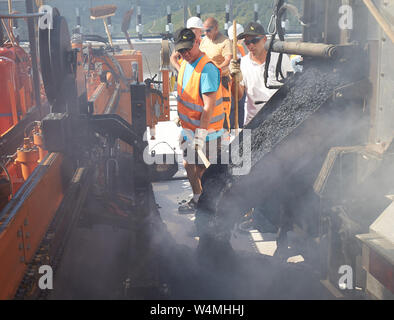 Zeltingen Rachtig, Deutschland. 24. Juli, 2019. Arbeitnehmer Asphalt der Straße Oberfläche des Hochmosel Brücke im Bau bei Temperaturen deutlich über 30 Grad Celsius. Es gibt keine schattigen Platz auf dem 160 Meter hohen Gebäude über dem Moseltal. Quelle: Thomas Frey/dpa/Alamy leben Nachrichten Stockfoto