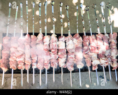 Viele Rohstoffe aufgespießt Shish Kebab (shashlyk) von Schweinefleisch sind auf Outdoor brazier mit heißem Kohle zubereitet Stockfoto