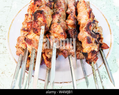 Viele heiß gekocht aufgespießt Shish Kebab (shashlyk) von Schweinefleisch close-up auf die Platte am Tisch im Freien Stockfoto